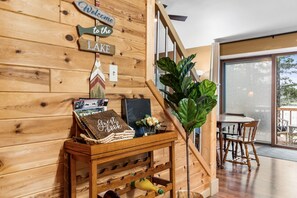 A wooden wall with a welcome sign, a guest book, and a small table with a plant and a bottle. - Lakefront on Lake Wequas | Private Beach, Dock + Kayaks (Gaylord)