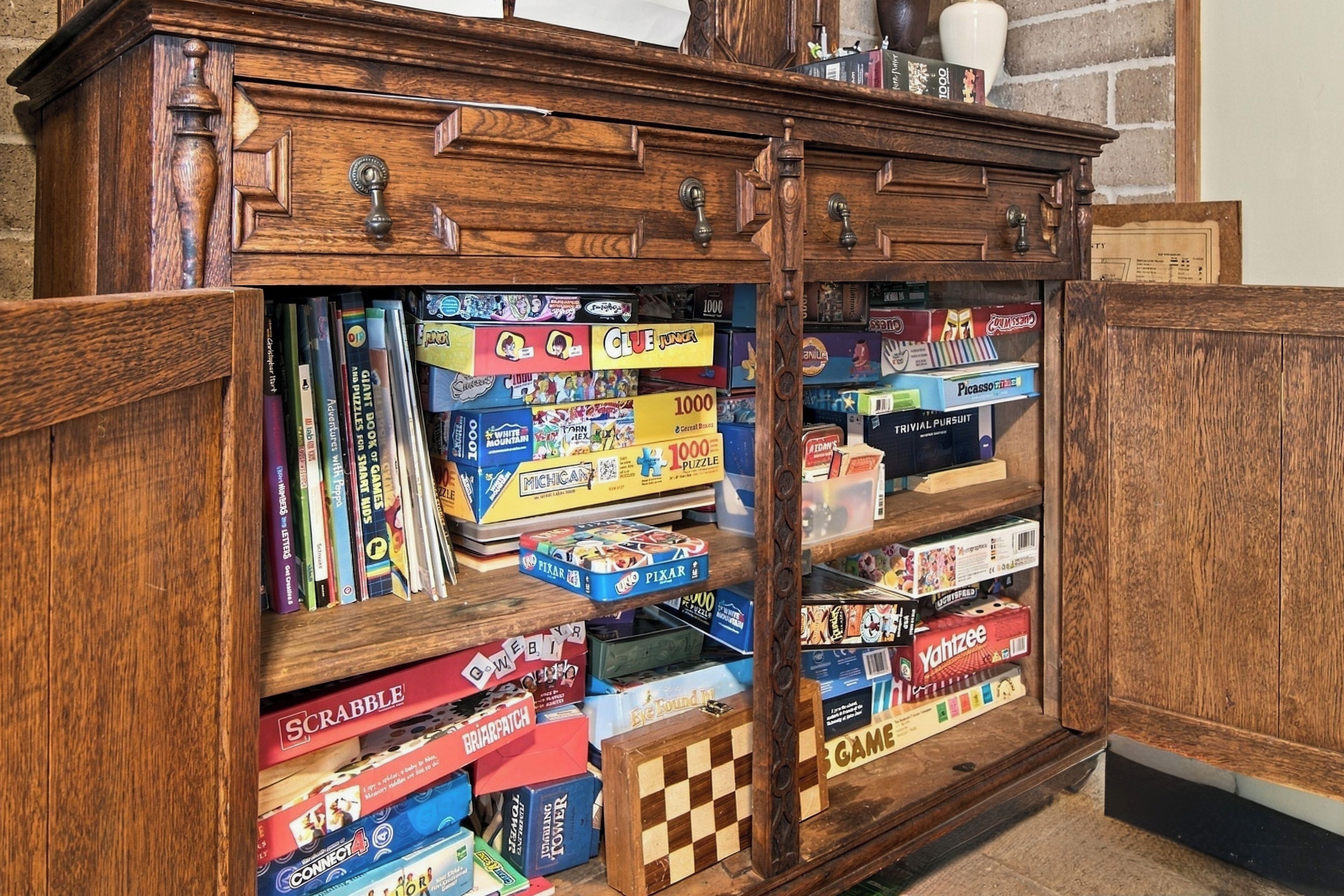 A wooden cabinet with multiple compartments containing various board games and puzzles.