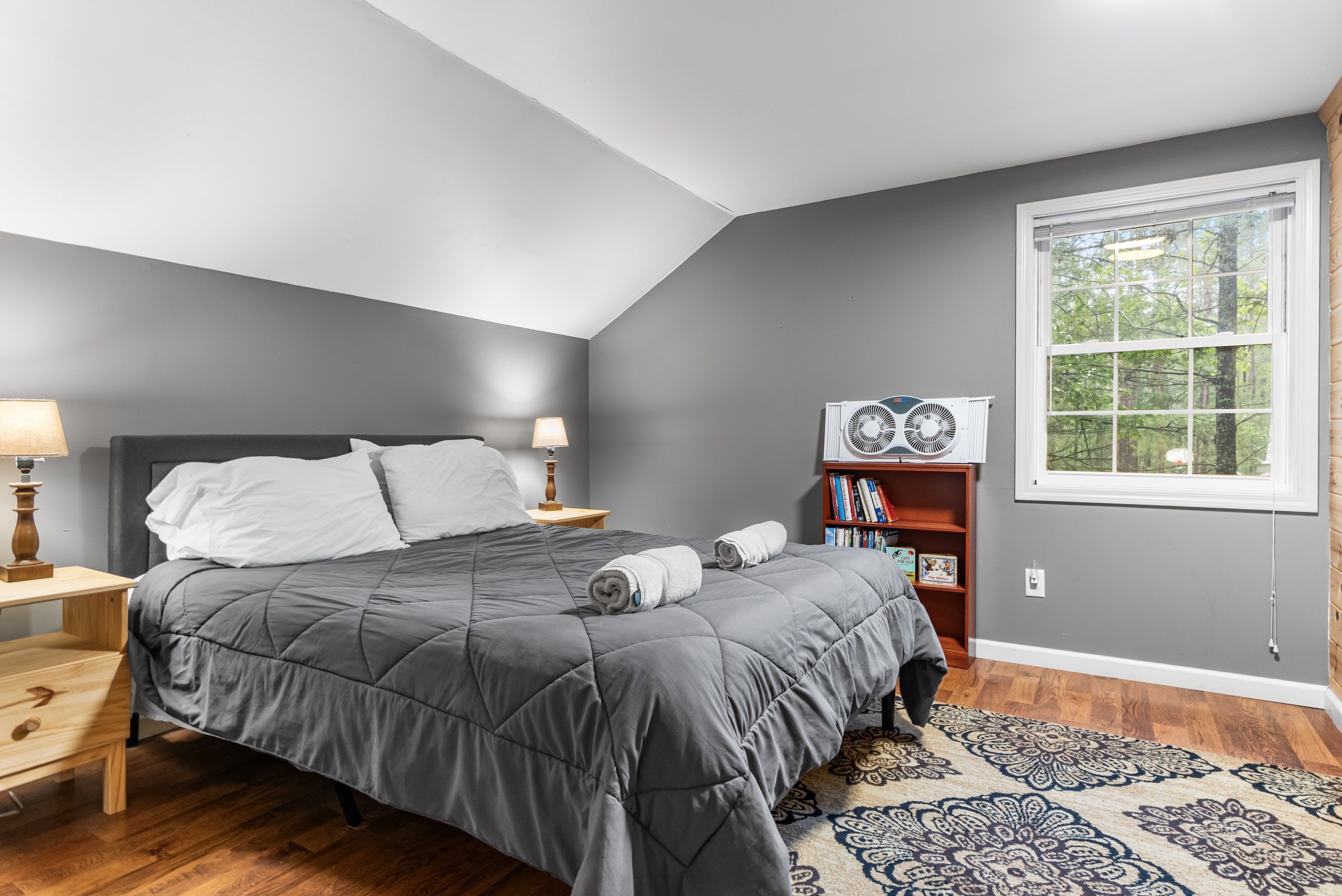A bedroom with a bed, nightstands, a lamp, a bookshelf, and a window.
