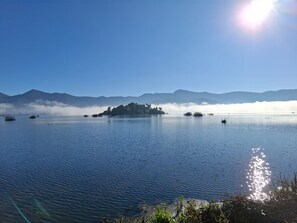 A calm lake with a small island in the center, surrounded by mountains and a clear sky.