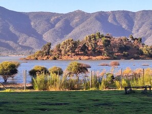 A lake with a grassy foreground and a forested hill in the background.