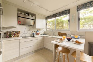 A modern kitchen with a marble countertop, wooden cabinets, a built-in oven, and a window with a view of trees. - Kensington 2-bed Near Notting Hill With Garden (London)