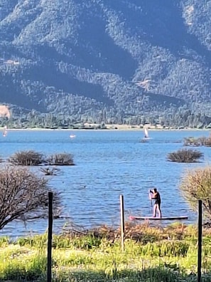A lake with a person on a paddleboard, surrounded by greenery and hills.