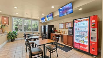 A restaurant with tables, chairs, a Coca-Cola vending machine, and a kitchen area.