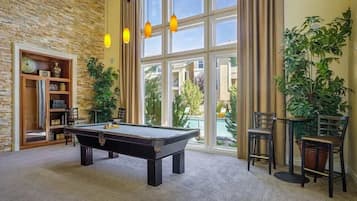 A pool table in a room with large windows, a bookshelf, and potted plants.