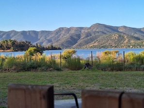 A view of a lake with mountains in the background, a grassy area in the foreground, and two wooden benches.
