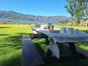 A picnic table set up on a grassy area with a lake and mountains in the background.