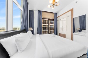 A hotel room with a large bed, a wardrobe, a mirror, a balcony with a view of the city, and a chandelier. - Stayshort - Peaceful 2-bedroom in Al Furjan That Sleeps 6 (Dubai)