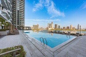 A rooftop swimming pool with lounge chairs, a view of the city skyline, and a clear sky. - Stayshort - Stunning Beachfront 3-bedroom Apartment Sleeps 5 With Infinity Pool Skyline Views Private Beach Access (Dubai)