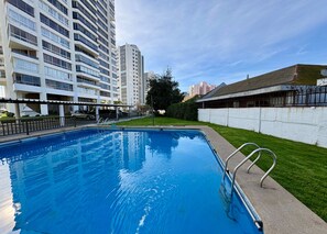 Ein Schwimmbecken mit Metallleiter, umgeben von einer weißen Mauer und einer Rasenfläche.