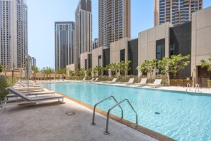 A swimming pool with lounge chairs and a modern building in the background. - Stayshort - Stylish 4-bedroom Oasis in Peaceful Creek Harbour (Dubai)