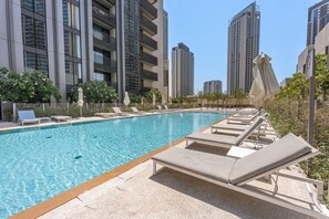 A swimming pool with lounge chairs and umbrellas, surrounded by high-rise buildings. - Stayshort - Stylish 4-bedroom Oasis in Peaceful Creek Harbour (Dubai)