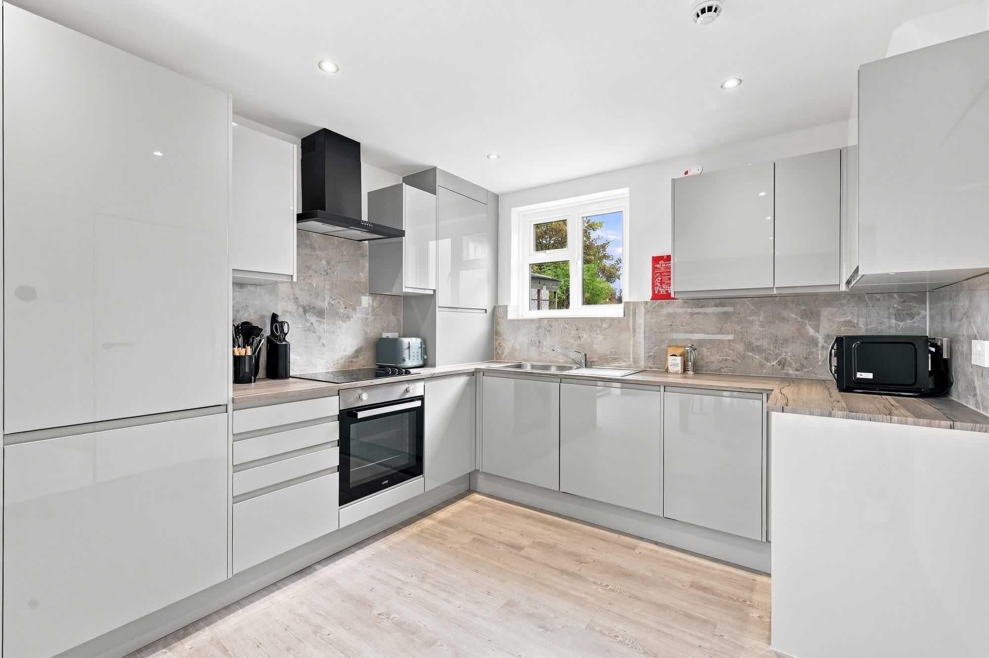 A modern kitchen with white cabinetry, a built-in oven, a microwave, and a window providing natural light.