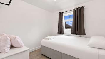 A bedroom with a bed, a window with curtains, a bedside table with pillows, and a ceiling light fixture.