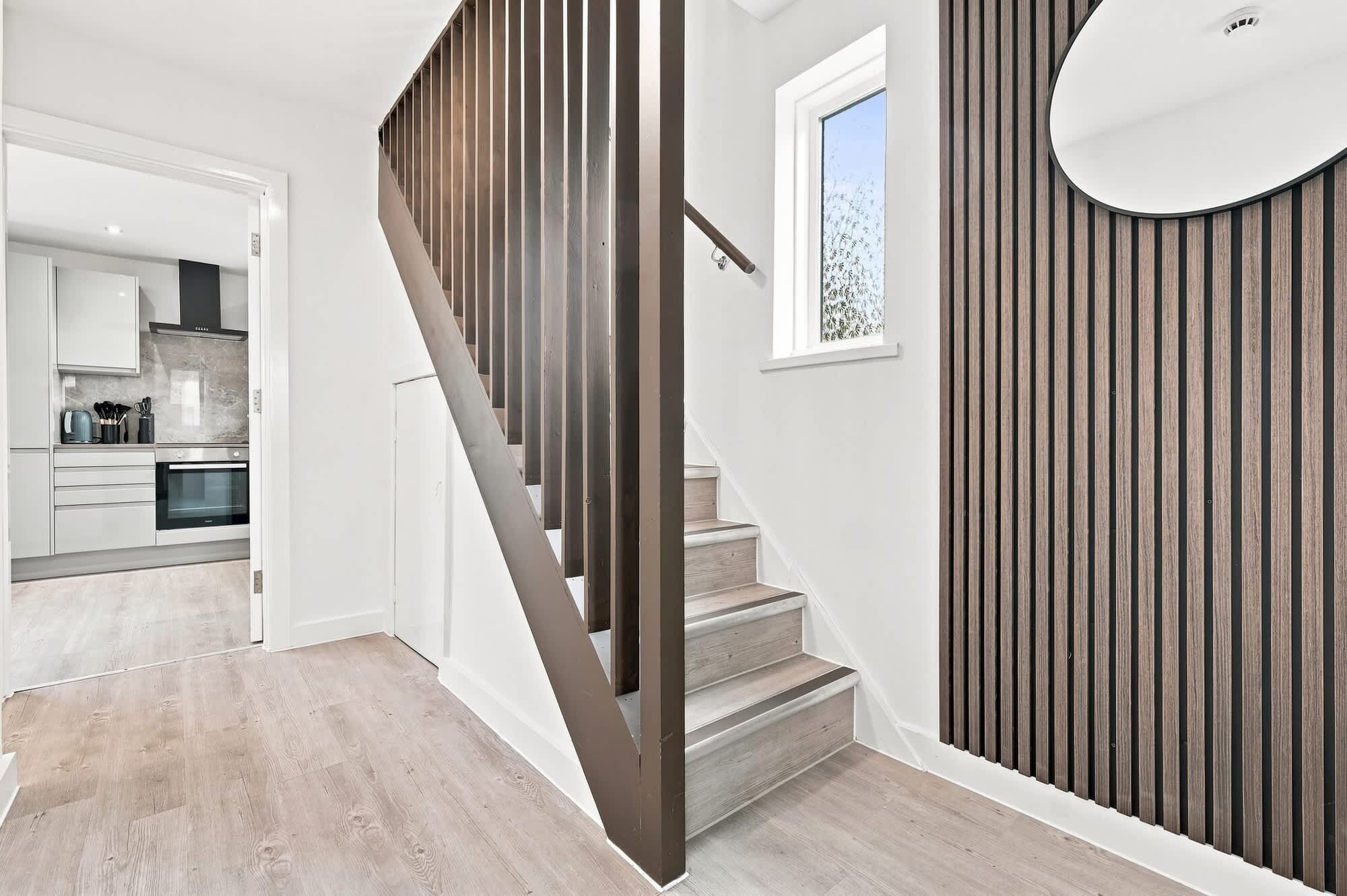 A staircase with wooden railings leading to a kitchen area.