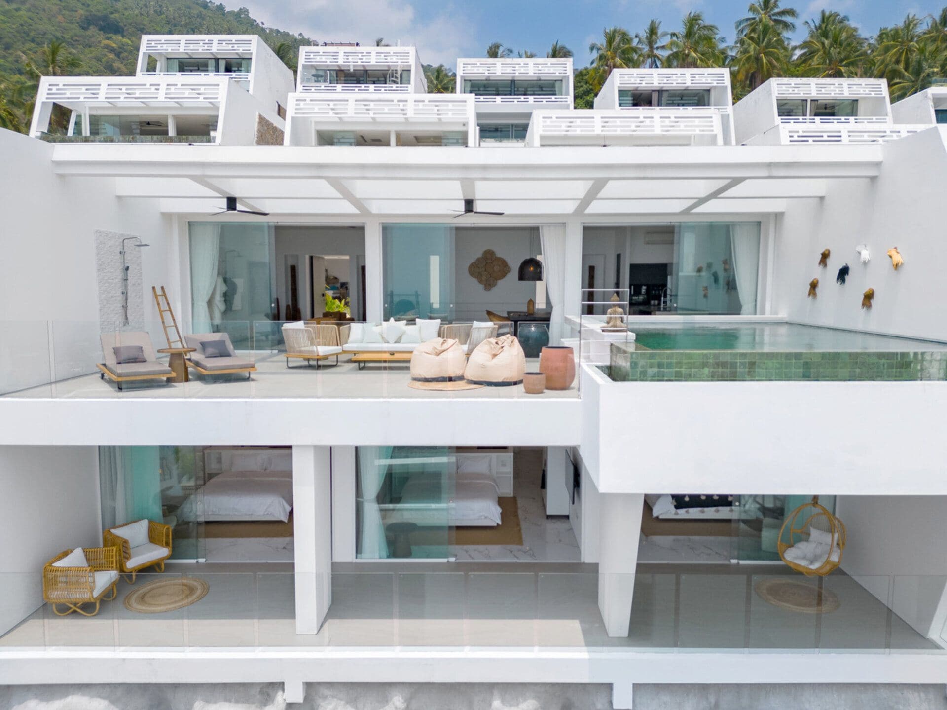 Un hôtel moderne à plusieurs étages, doté d’une piscine sur le toit, de balcons entièrement vitrés et offrant une vue sur un paysage tropical.