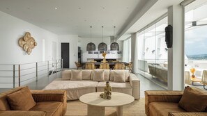 A modern living room with a large sofa, a round coffee table, and a Buddha statue. There is a dining area with a table and chairs in the background. - 5 Star Golden Lotus Villas – Hilltop Luxury (Chang Wat Surat Thani)
