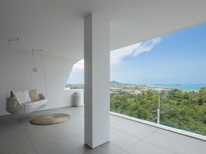 Ein modernes Zimmer mit einem Hängekorbstuhl, einem runden Teppich und einem großen Fenster mit Blick auf eine Küstenlandschaft.