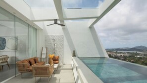 Ein modernes Interieur mit Glasdecke, einer Sitzecke mit Korbmöbeln, einer Steinwand, einer kleinen Buddha-Statue und Blick auf Stadt und Berge.