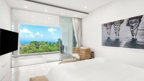 Una camera da letto moderna con un letto grande, una televisione, una poltrona in vimini e vista sull'oceano.