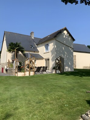 A two-story house with a patio, a stone wall, and a palm tree. - Guest Room “L’hermine Blanche” with Wi-Fi (Calorguen)