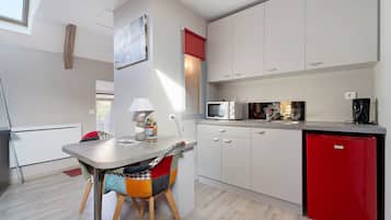A compact kitchen with white cabinets, a red refrigerator, and a dining area with a table and chairs.