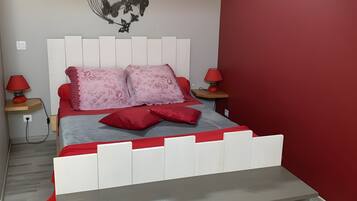 Un dormitorio con una cama, una pared roja, un tragaluz y una mesita de noche con una lámpara.