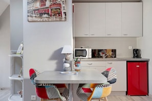 A compact kitchen with a dining table, chairs, a microwave, and a red refrigerator.