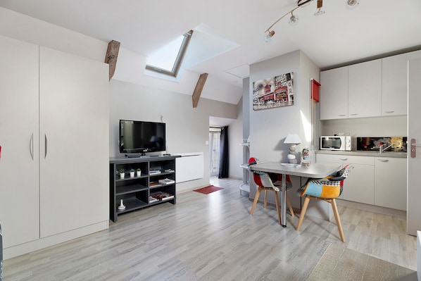 A modern kitchen with a built-in microwave, a dining area with a table and chairs, and a TV on a stand.