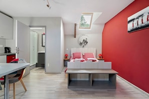A modern bedroom with a bed, bedside tables, a red accent wall, and a skylight.