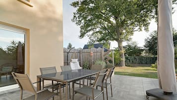 Une terrasse extérieure avec une table et des chaises en verre, un fauteuil suspendu et un espace abrité.