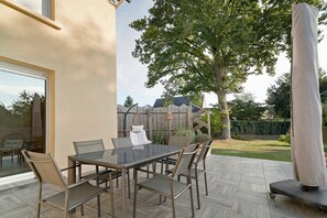 An outdoor patio with a glass table and chairs, a hanging chair, and a covered area.