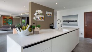 Una cocina moderna con una isla grande, muebles blancos y un lavamanos en la isla. Hay plantas decorativas y un jarrón con flores sobre la isla.