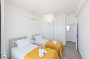 A hotel room with two beds, a wardrobe, a hanging light fixture, and a door leading to another room. - Luxury 5 Star Cottage – Prime Protaras 1047 (Famagusta)