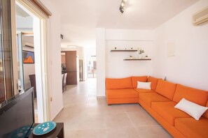 A modern living room with a sectional sofa, a dining area with a table and chairs, and a kitchen in the background. - Luxury Escape in Kapparis Paradise 1053 (Famagusta)