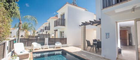 A residential area with a swimming pool, outdoor seating, and a view of neighboring houses.