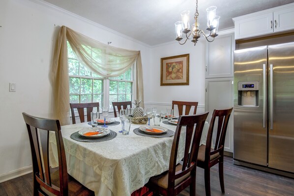Comedor con mesa dispuesta para cuatro, sillas, candelabro, refrigerador y ventana con cortinas.