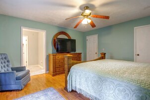 Un dormitorio con una cama, un televisor sobre una cómoda, una silla y un ventilador de techo.