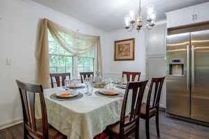 Comedor con mesa dispuesta para cuatro, sillas, candelabro, refrigerador y ventana con cortinas.