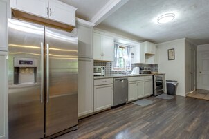 Cozinha moderna com eletrodomésticos de aço inoxidável, armários brancos e painel de azulejos.