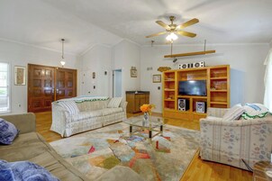 Una sala de estar con sofá, sillón, mesa de centro de vidrio y televisor sobre un mueble de madera.