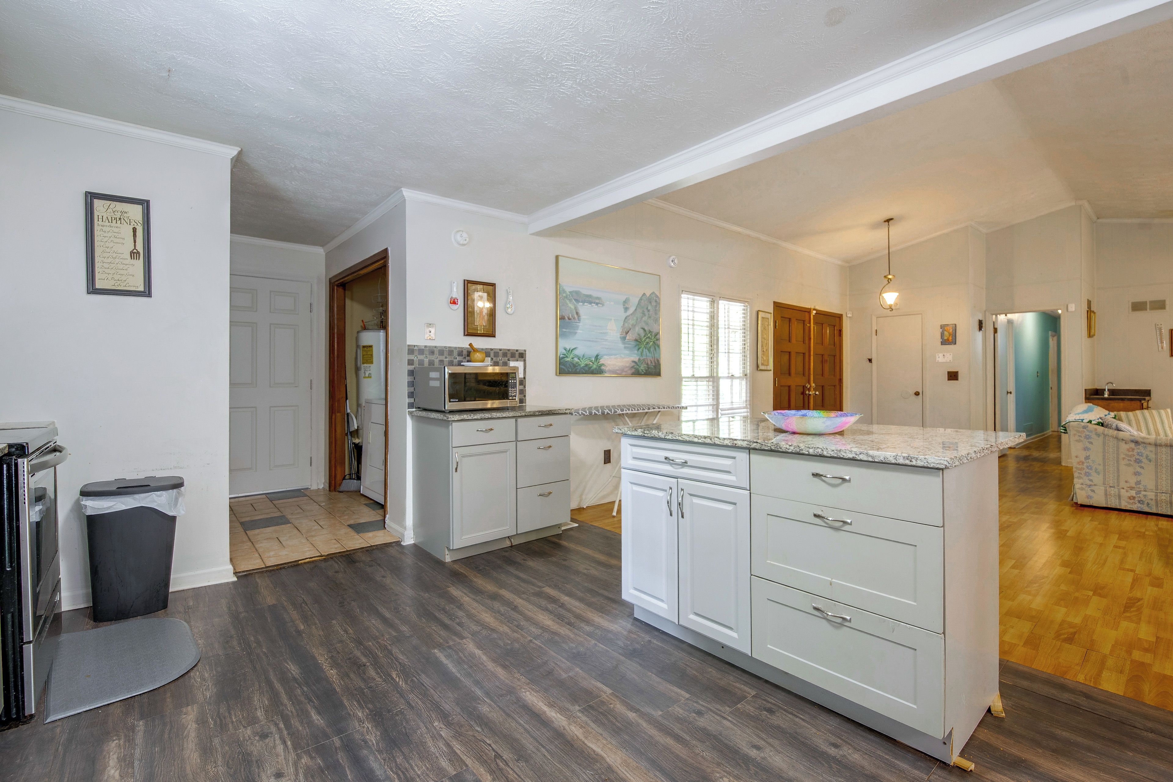 A spacious kitchen with a central island, wooden flooring, and a view into the living area.