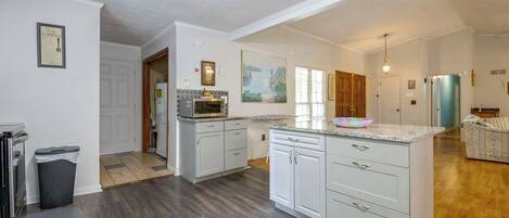 A spacious kitchen with a central island, wooden flooring, and a view into the living area.