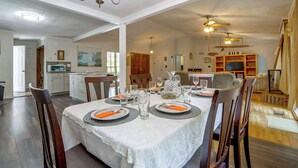 Een eethoek met een tafel voor vier personen, stoelen, een kroonluchter en een plafondventilator.