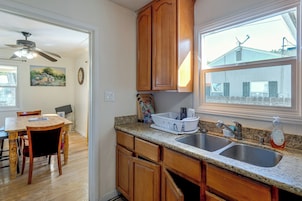 Una cocina con armarios de madera, encimera de granito, pileta doble y ventana con vista a una casa y un molino.