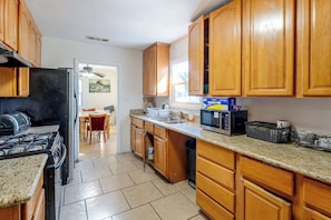 A kitchen with wooden cabinets, a stove, a microwave, and a dining area with chairs and a table. - Cozy Stockton Home Close to UOP & Miracle Mile (Stockton)