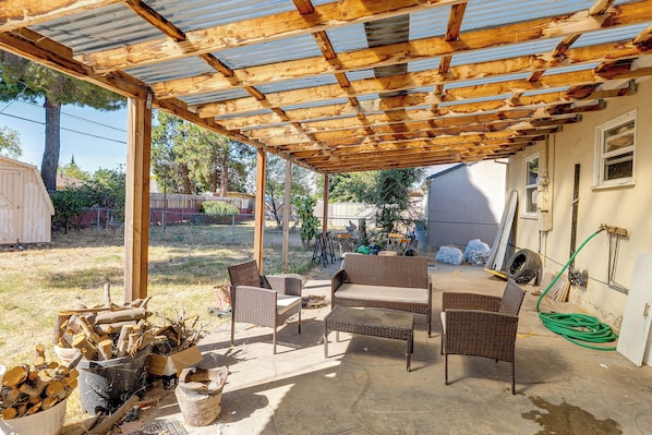 An outdoor patio area with a wooden pergola, wicker furniture, and a firewood storage. - Cozy Stockton Home Close to UOP & Miracle Mile (Stockton)