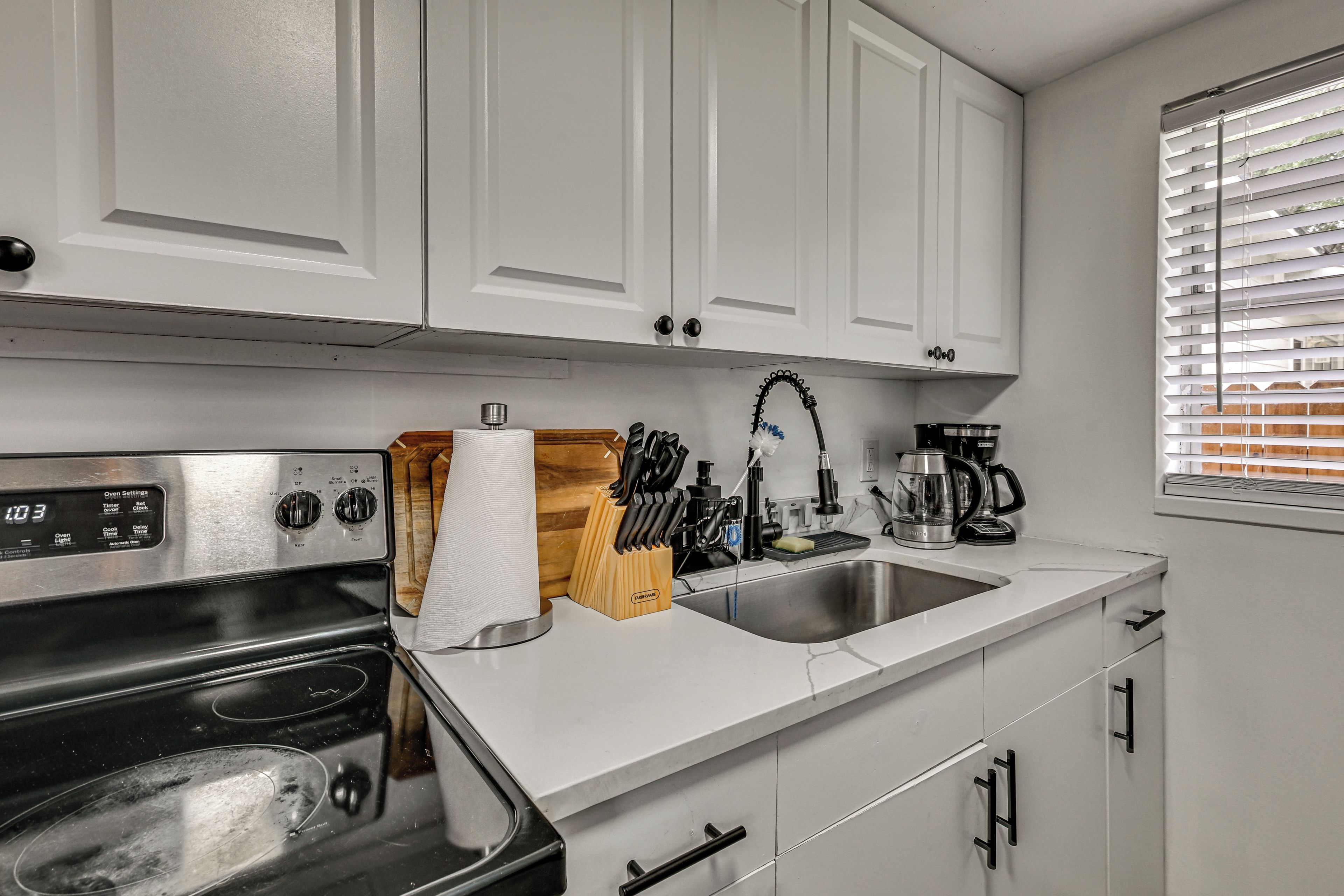 A kitchen with white cabinets, a stainless steel stove, a sink, and a window with blinds.