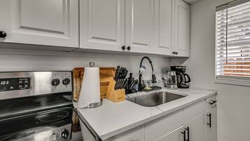 A kitchen with white cabinets, a stainless steel stove, a sink, and a window with blinds.