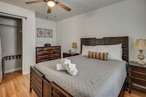 Quarto com cama de madeira, mesa de cabeceira, cômoda, ventilador de teto e uma obra de arte pendurada na parede.